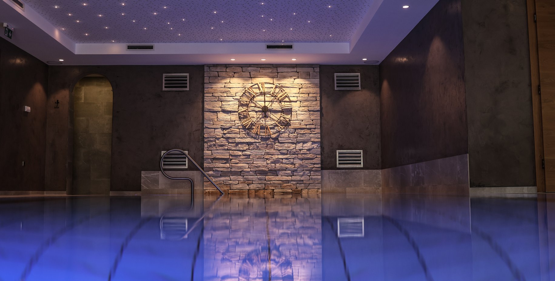 Blauer Indoorpool mit Sternenhimmel und antiker Uhr an der Wand